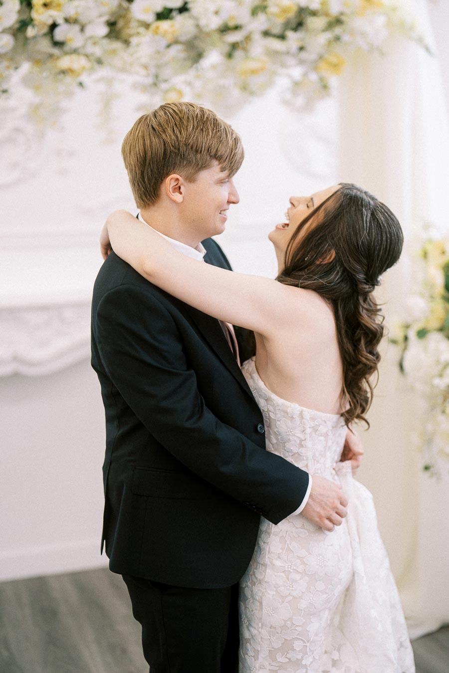A newlywed couple embracing on their wedding day, with the bride in a white lace gown and the groom in a black suit,