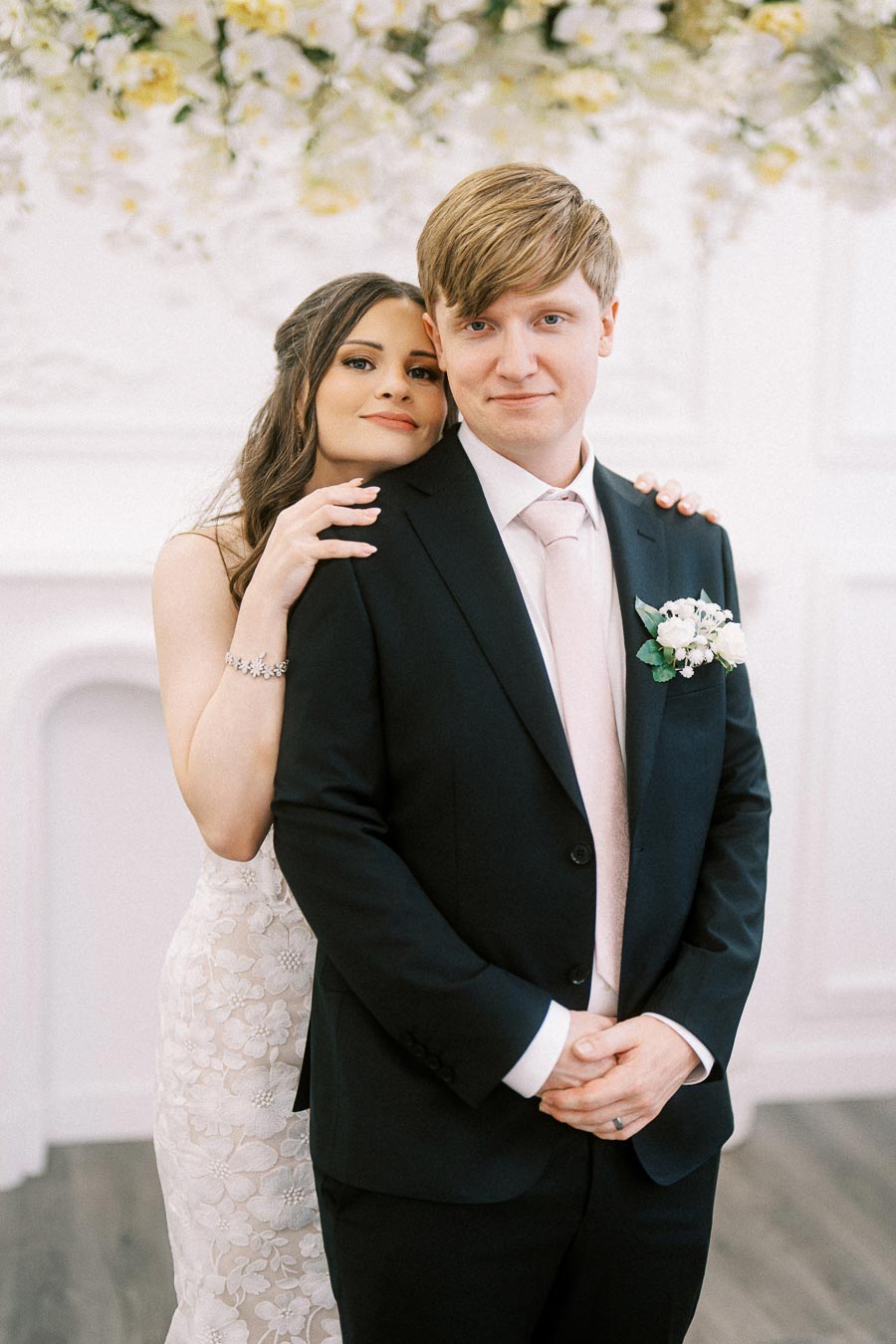 A joyful couple on their wedding day, with the bride in a lace gown embracing the groom in a black suit, standing in a