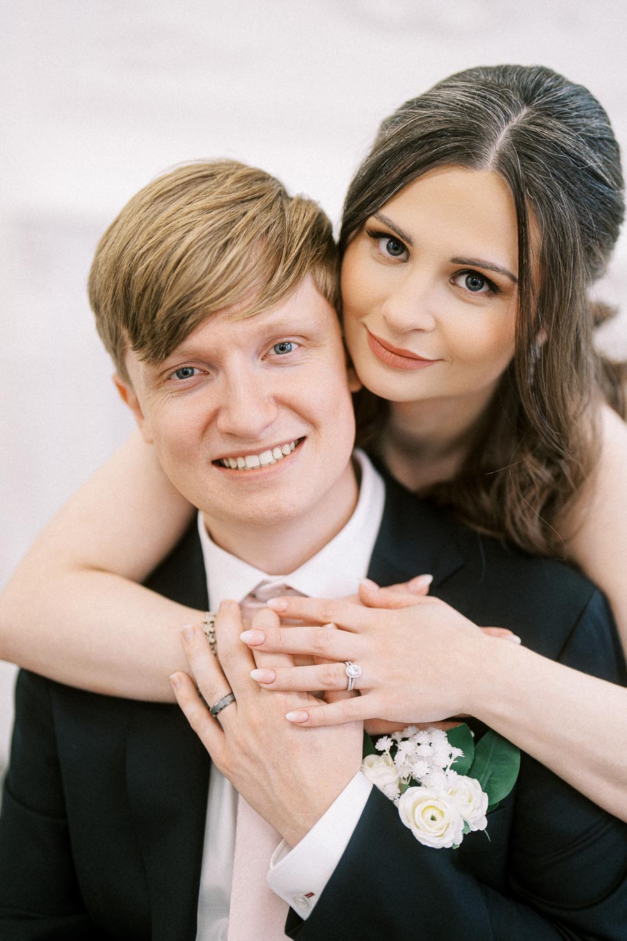 Happy couple posing on their wedding day, showcasing engagement and wedding rings, with elegant attire and floral