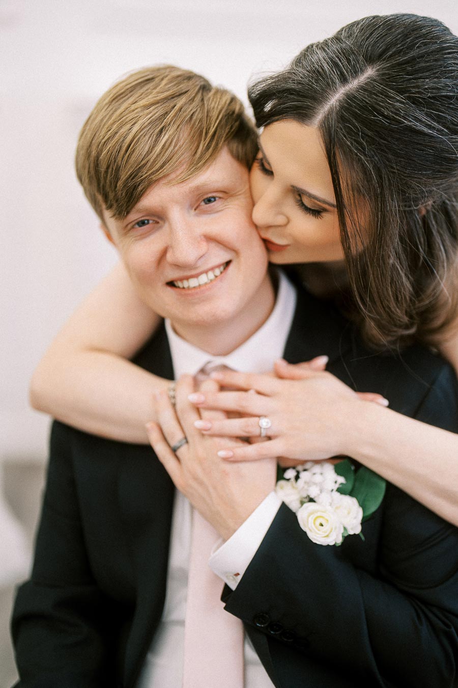 A happy couple on their wedding day, with the bride kissing the groom's cheek, both smiling warmly.