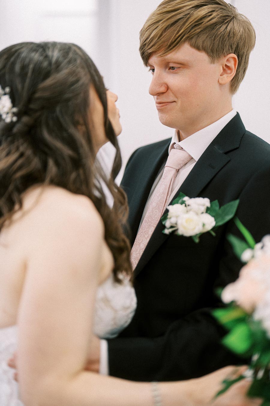 Wedding couple gazing at each other lovingly, with the groom in a black suit and pink tie and the bride in a white dress,