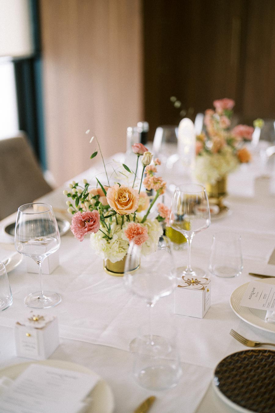 Elegant table setting for a formal event, featuring a centerpiece with orange and pink flowers, crystal wine glasses, and