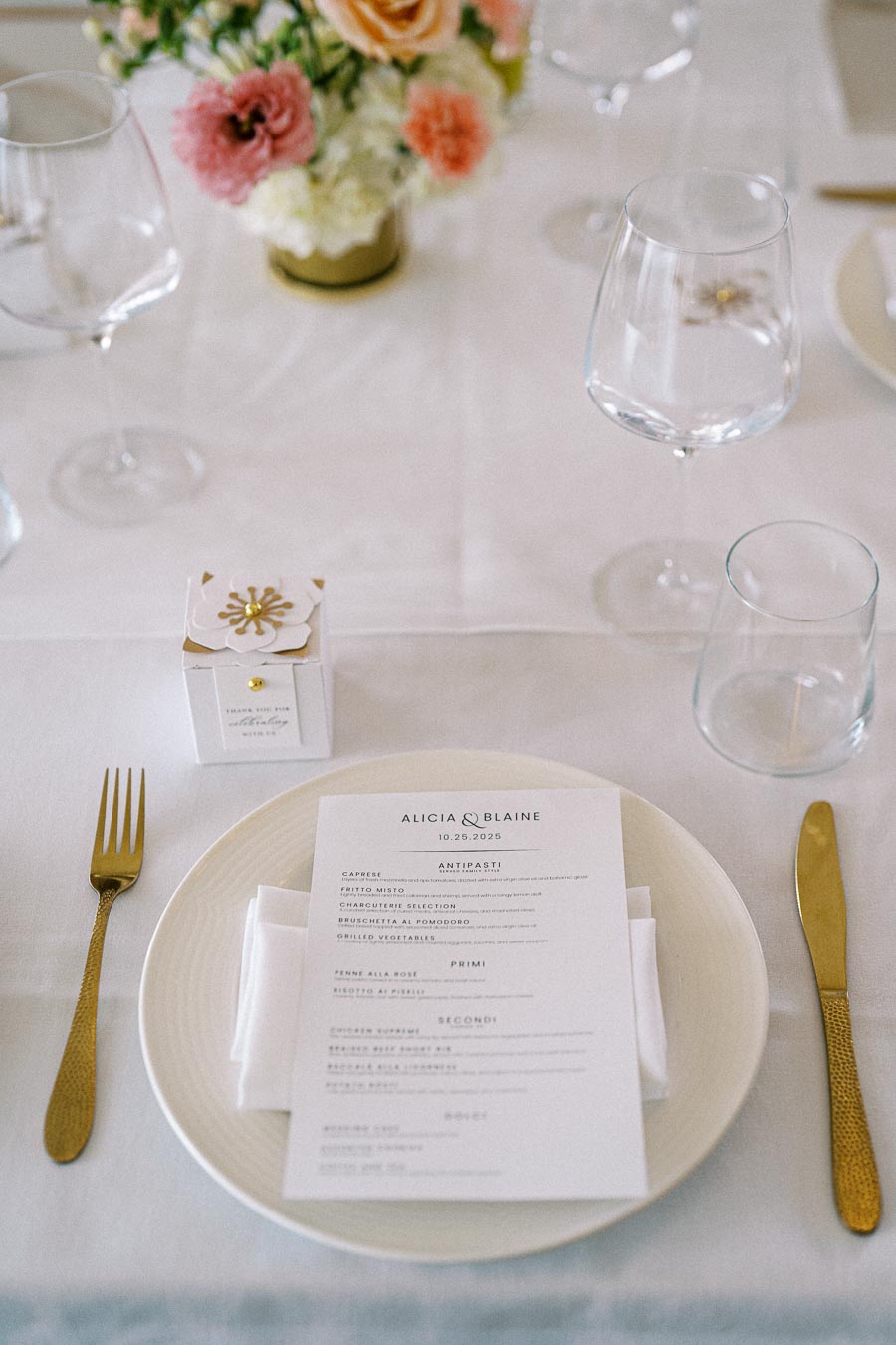 Elegant wedding table setting featuring a white plate with a personalized menu card, gold silverware, and delicate floral