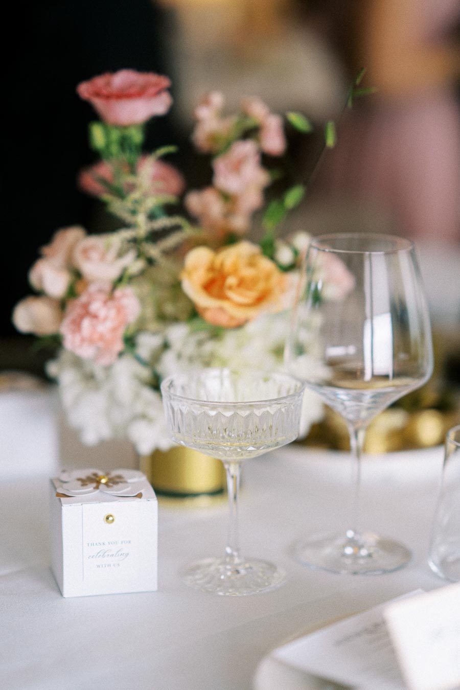 Elegant wedding table setting featuring pastel flower arrangement, crystal glassware, and a small gift box on a white