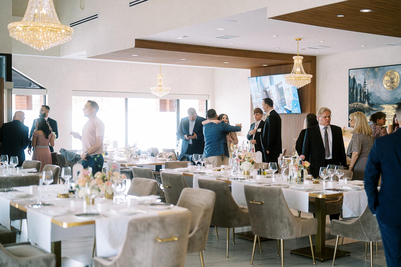Elegant dining room set up for an event, with guests socializing near tables adorned with white tablecloths and floral