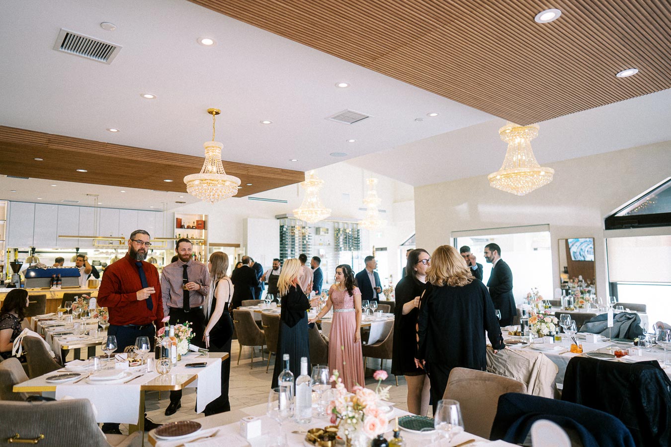 Elegant restaurant interior hosting a lively social gathering with guests mingling near beautifully set tables, featuring