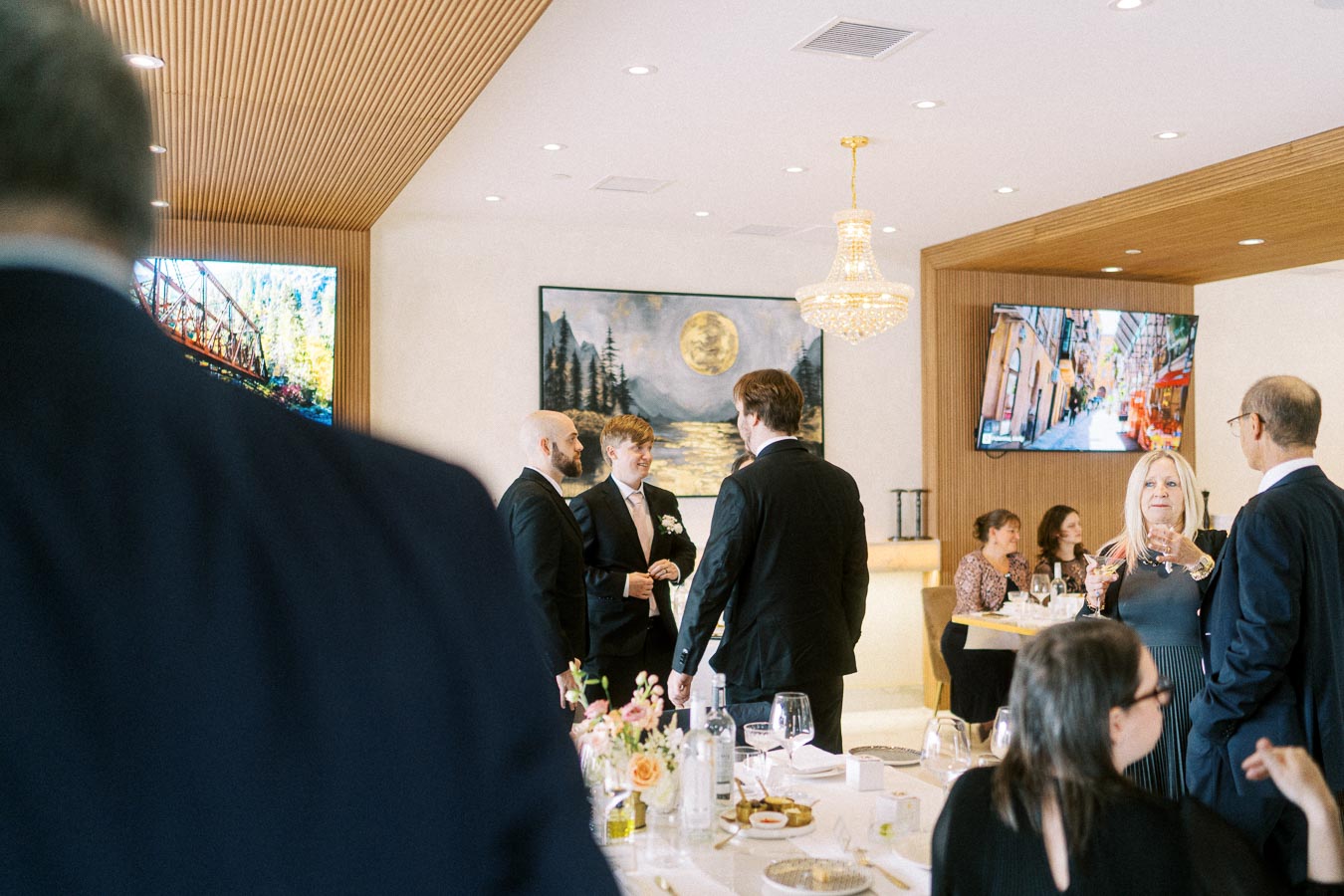 Elegant indoor gathering with guests in formal attire, discussing under a chandelier in a sophisticated venue adorned with