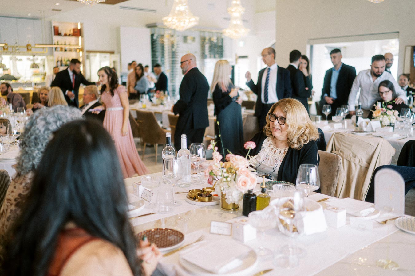A lively banquet scene with elegantly dressed guests socializing around decorated tables, featuring floral centerpieces and