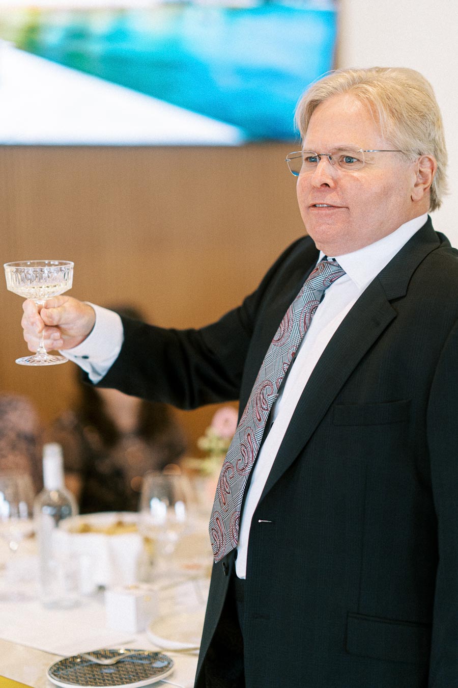 A man in a suit toasting with a crystal glass at a formal event.