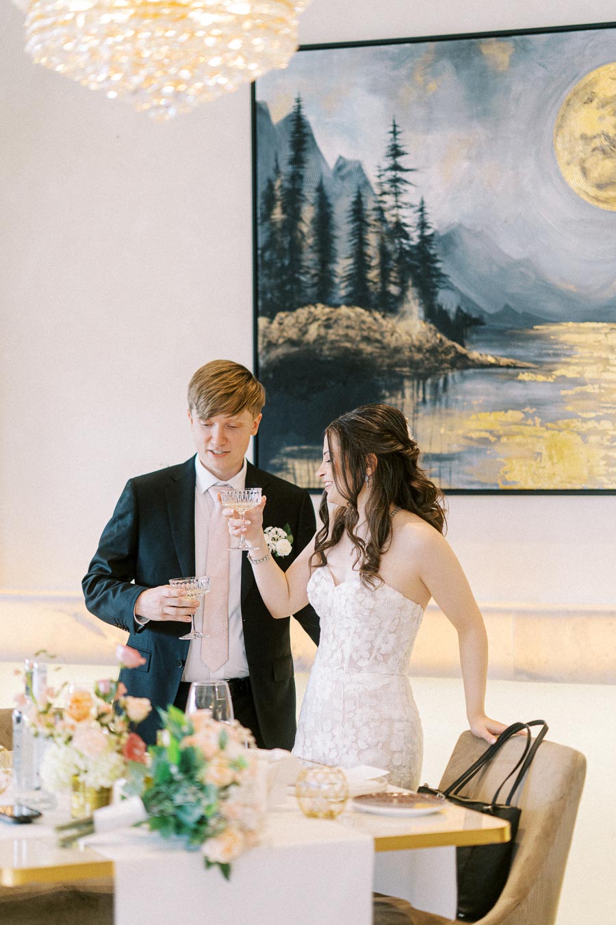 Elegant couple toasting at a wedding reception, wearing formal attire in a beautifully decorated room with a nature-inspired