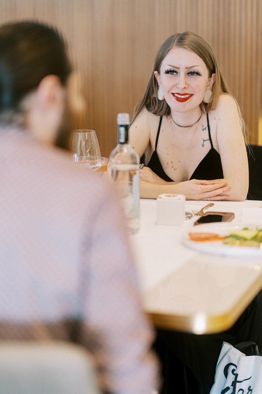 A woman sitting at a restaurant table, smiling and engaged in conversation, with a bottle of water and a cell phone in front