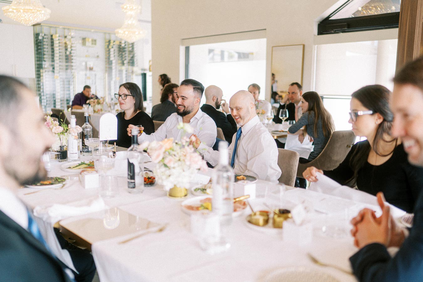 A group of people sitting at a table in a modern, elegant restaurant setting, enjoying a meal together. The table is set
