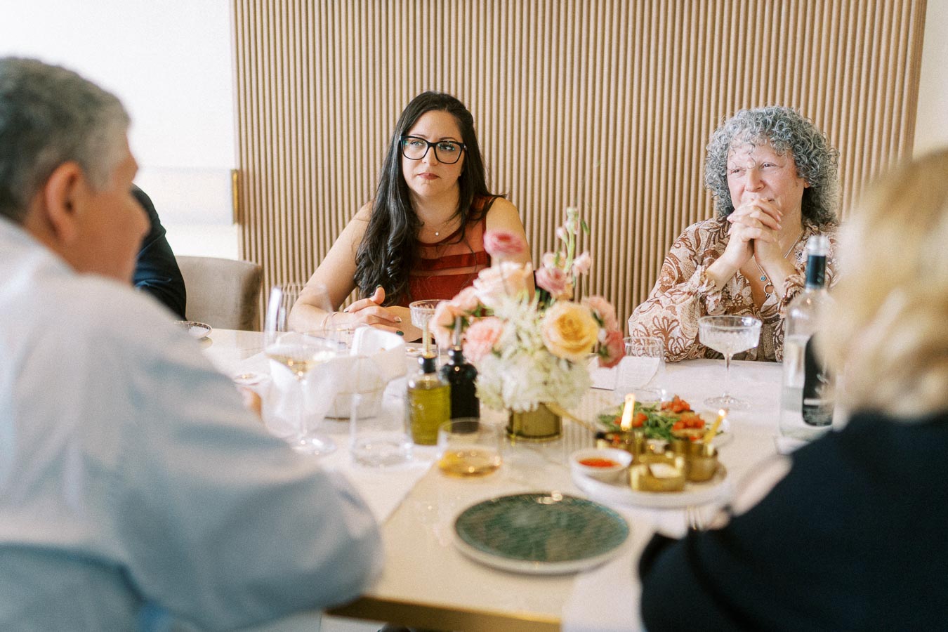 Group of people engaging in conversation around a elegantly set dining table, featuring a centerpiece of pink and yellow