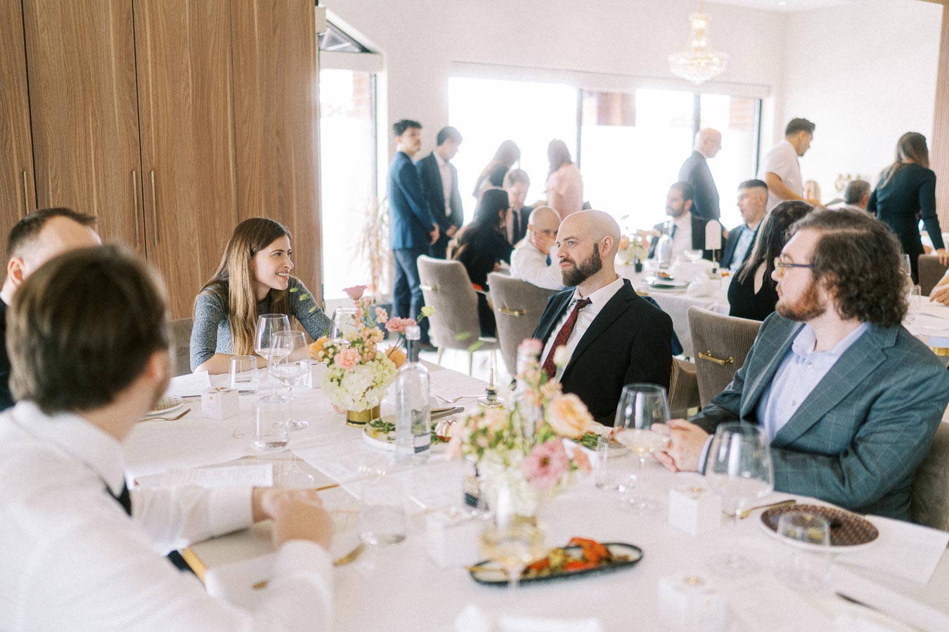Group of elegantly dressed people engaged in conversation at a formal dining event, with a beautifully set table featuring