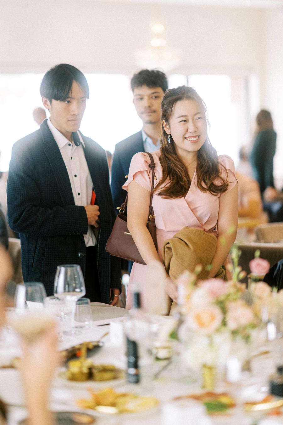 Three people standing and smiling at a elegant social gathering event, with a beautifully set table in the foreground.