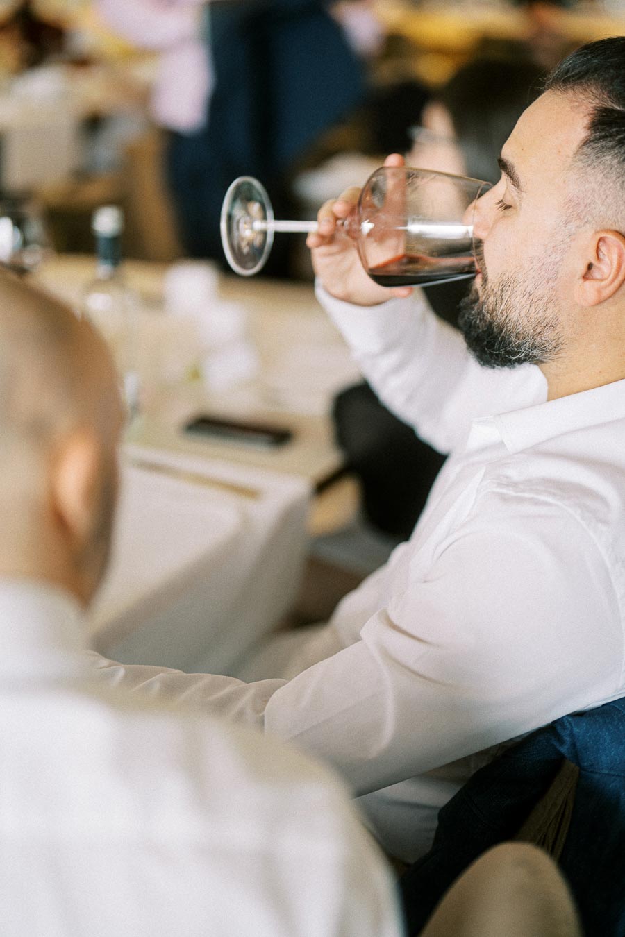 A person enjoying a glass of wine at a formal event, seated at a table with a white tablecloth, creating a relaxed and