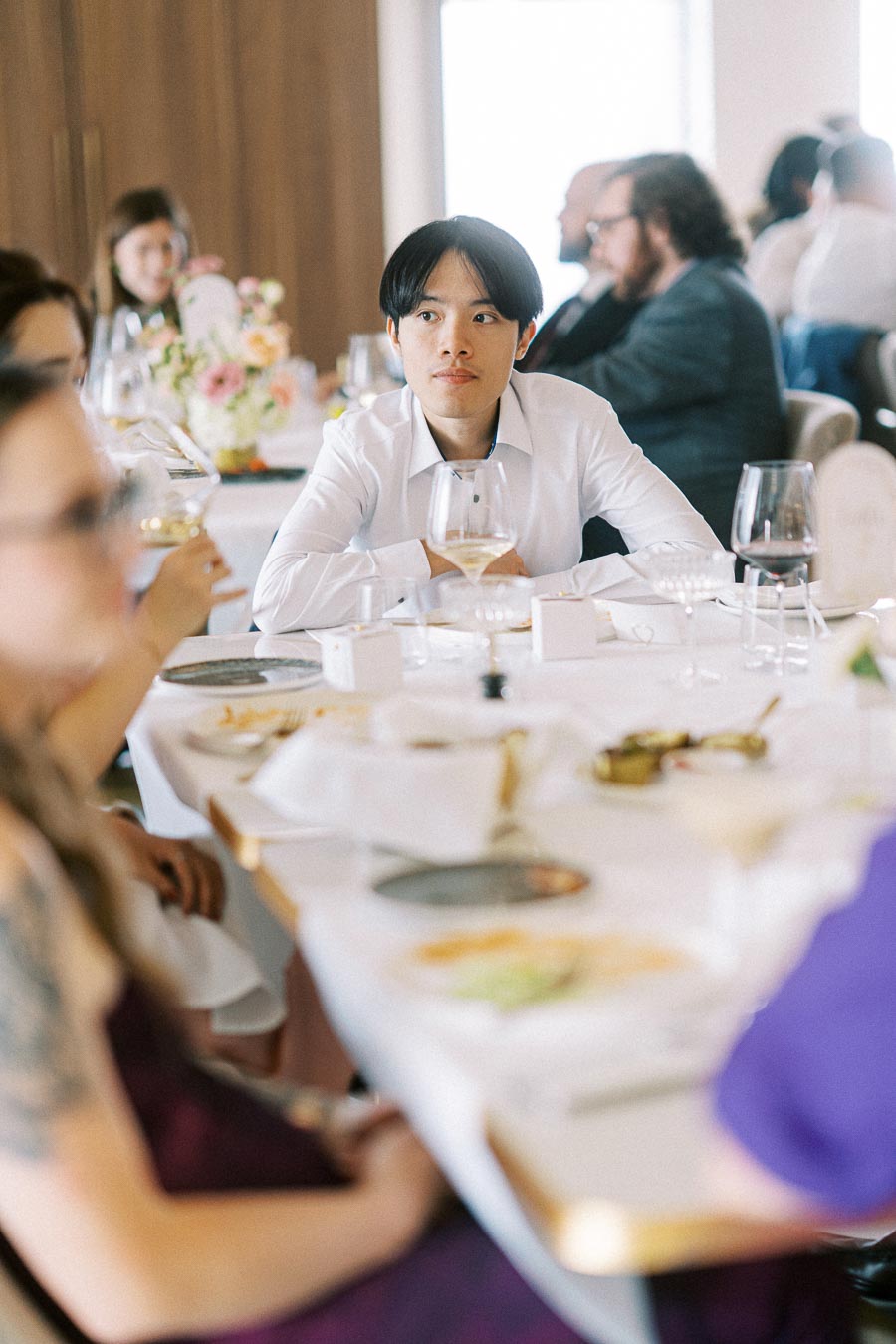 A person attentively listening at a formal dining table during a social gathering, surrounded by elegantly set plates and