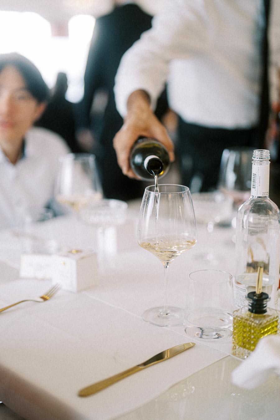 A waiter pouring white wine into a glass at an elegantly set restaurant table, featuring a crisp white tablecloth,