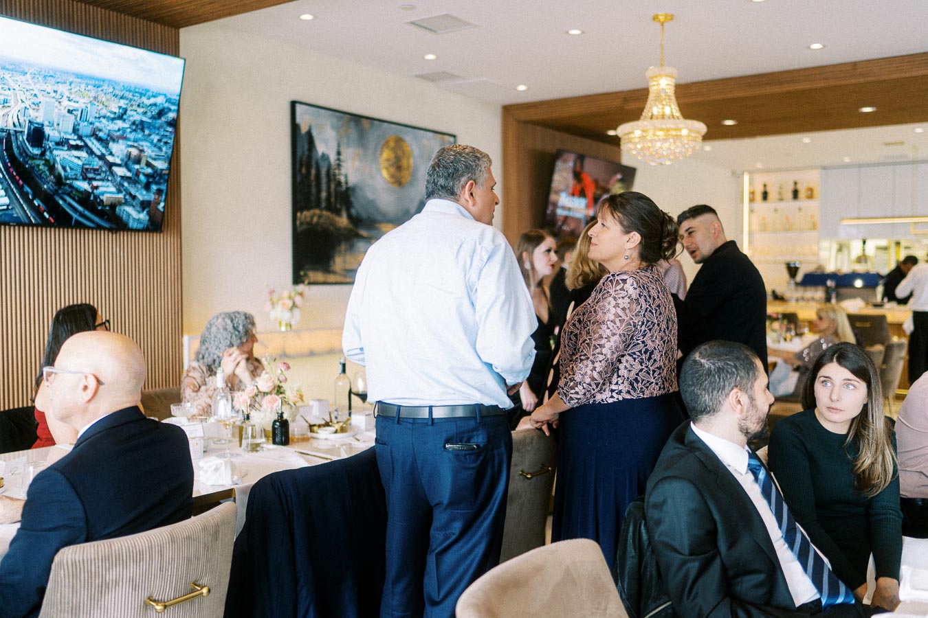 A group of people networking at a formal event in a modern restaurant setting, featuring elegantly set tables and a large