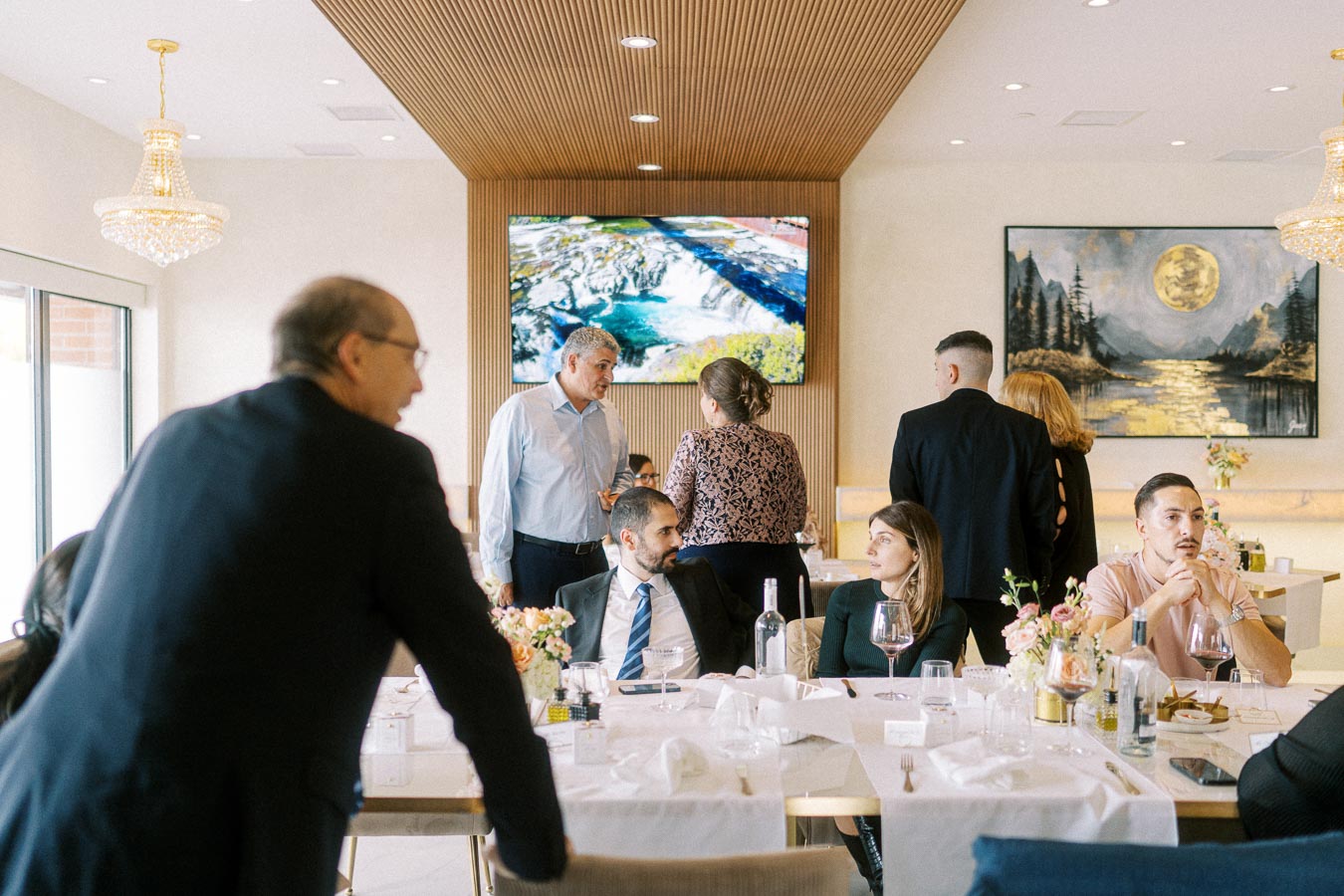 Group of people attending a formal gathering in a modern, elegant dining room with decorative art and floral arrangements;