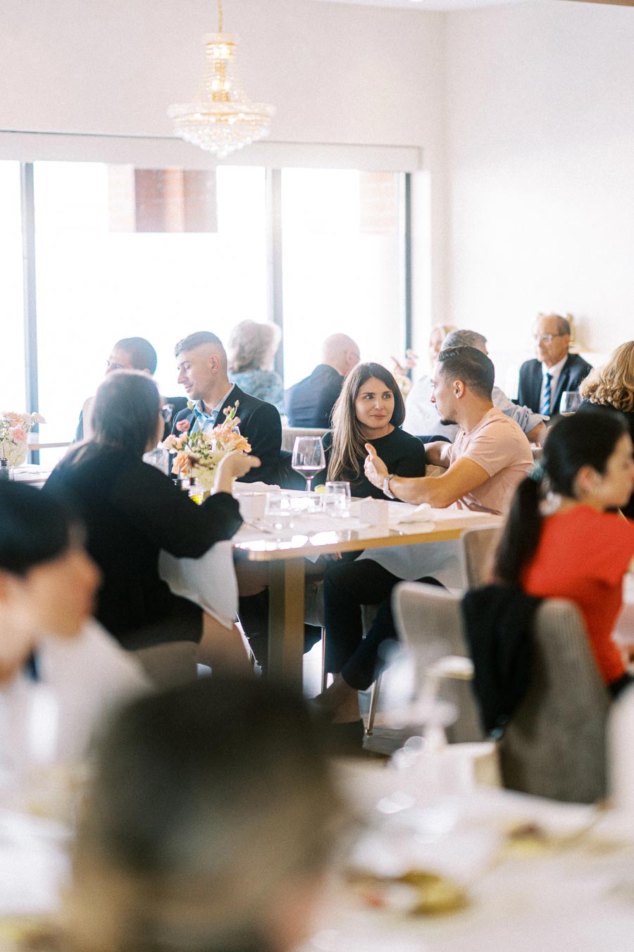 A lively restaurant scene with people enjoying a meal, engaged in conversation around a table, adorned with flowers and