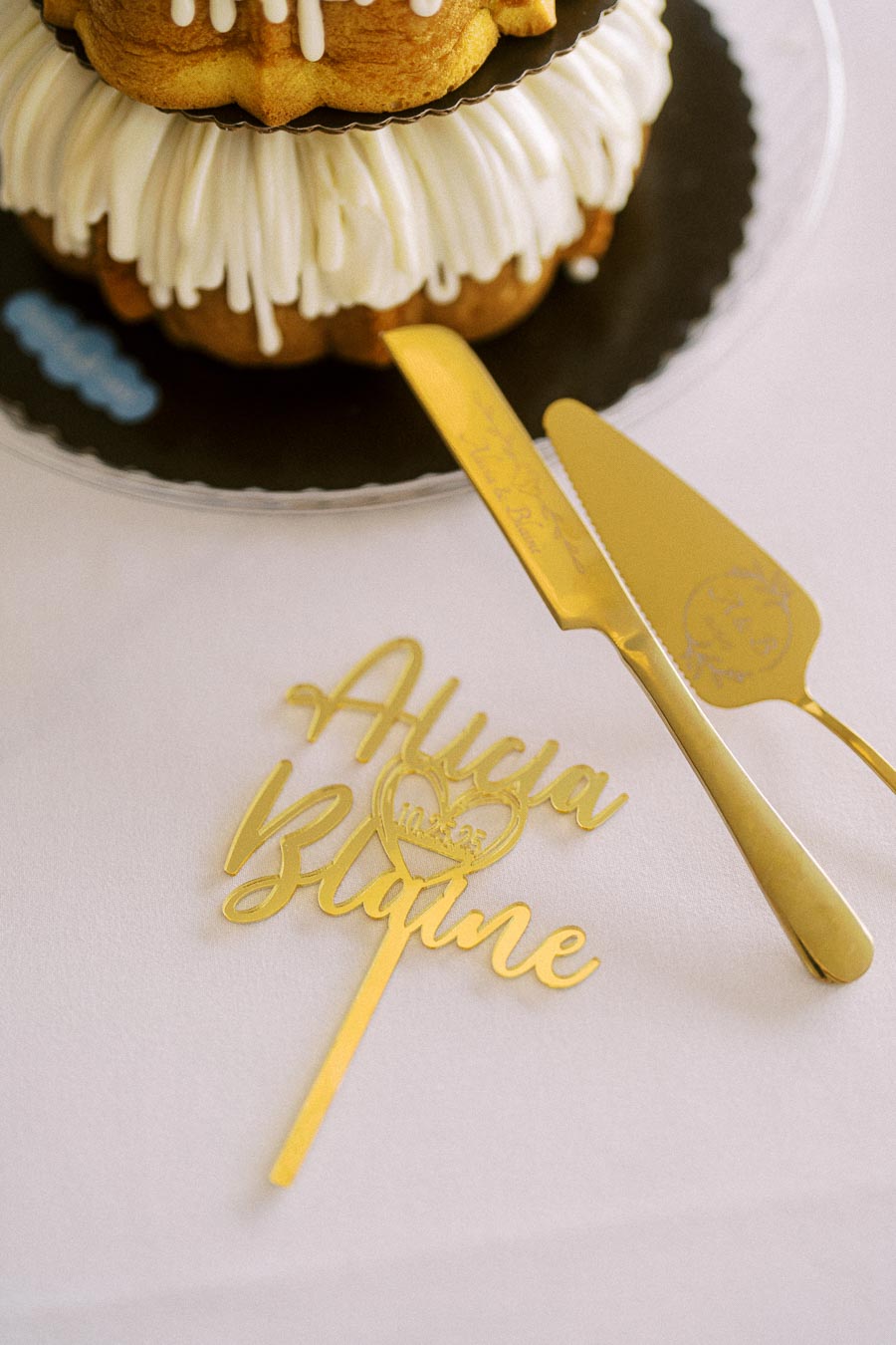 Elegant wedding cake on table with a decorative cream frosting design, accompanied by a personalized gold cake knife and