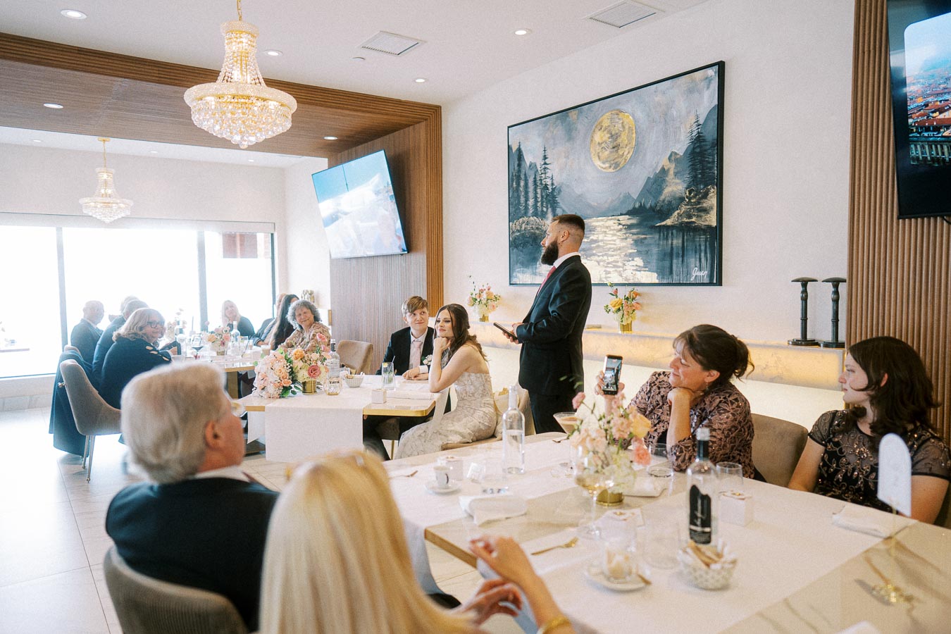 Elegant indoor wedding reception with guests seated around tables adorned with floral arrangements and elegant decor,