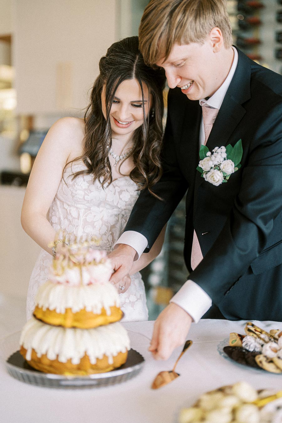 A bride and groom joyfully cutting their wedding cake together, featuring a three-tiered design with white icing,