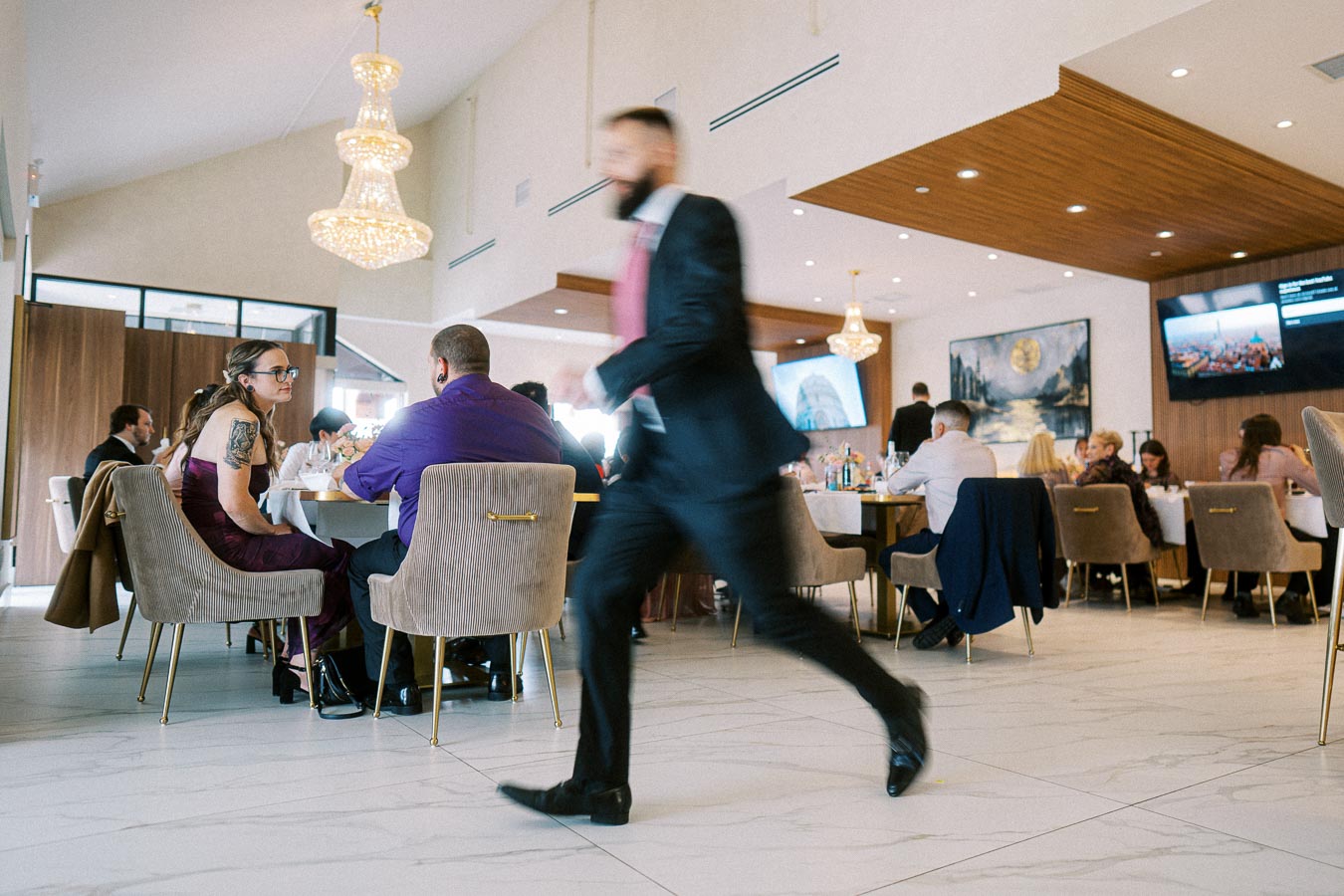 Elegant restaurant interior with guests seated at tables, beautifully lit by chandeliers, and a person in business attire