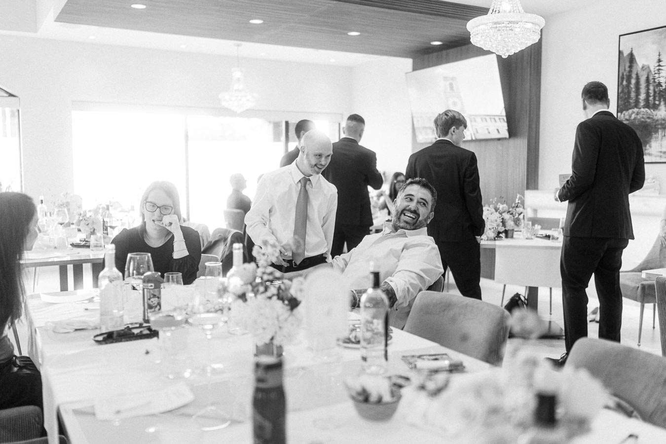 Black and white photo of a lively gathering at a dining table, featuring people in suits and casual attire sharing a