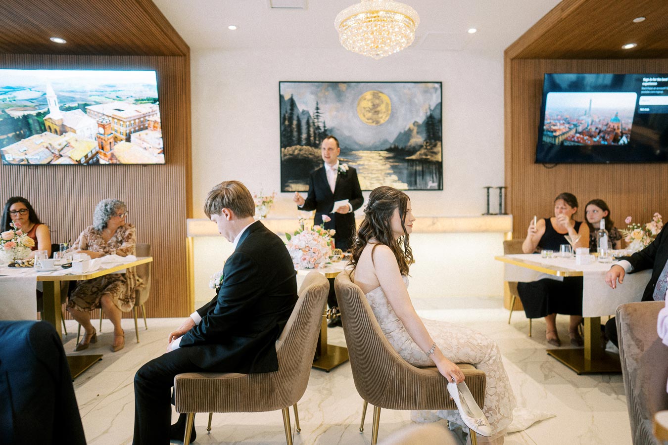 Wedding reception with bride and groom participating in a shoe game, seated back-to-back in an elegant venue with guests