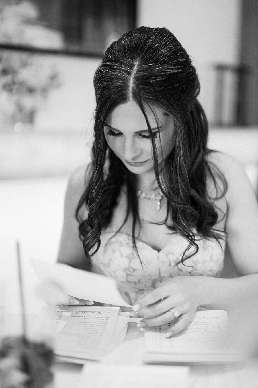 Black and white image of a woman in a floral dress reading documents, showcasing an elegant hairstyle and a delicate