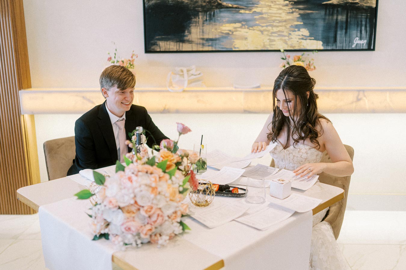 A couple signing documents at a decorated table during their wedding ceremony, surrounded by elegant floral arrangements and