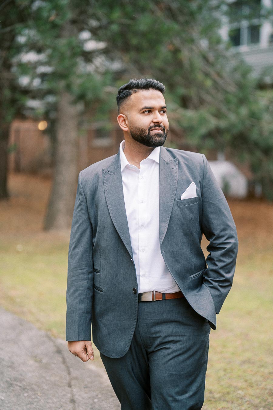 Confident man in a gray suit walking outdoors on a path with trees in the background