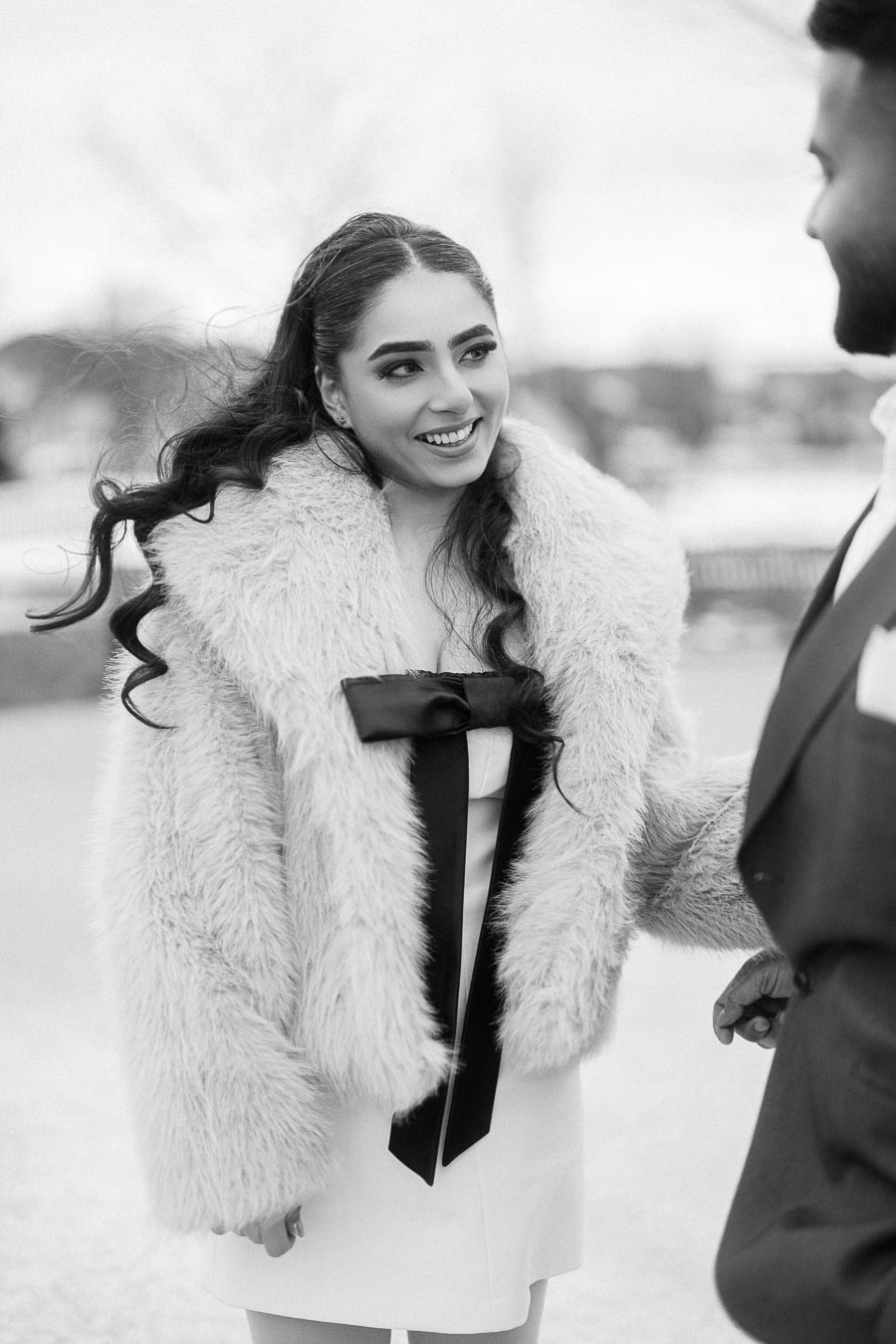 A woman in a fur coat smiles warmly at a man outdoors, black and white photograph.