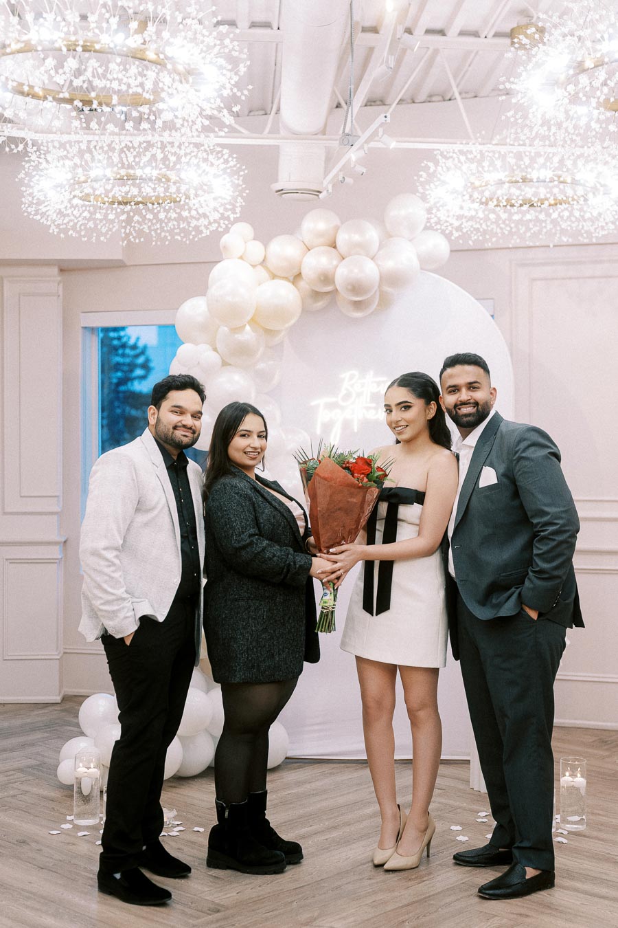 Group of friends at an elegant celebration with balloon decorations and floral arrangements, posing for a photo in a beautifully decorated venue.
