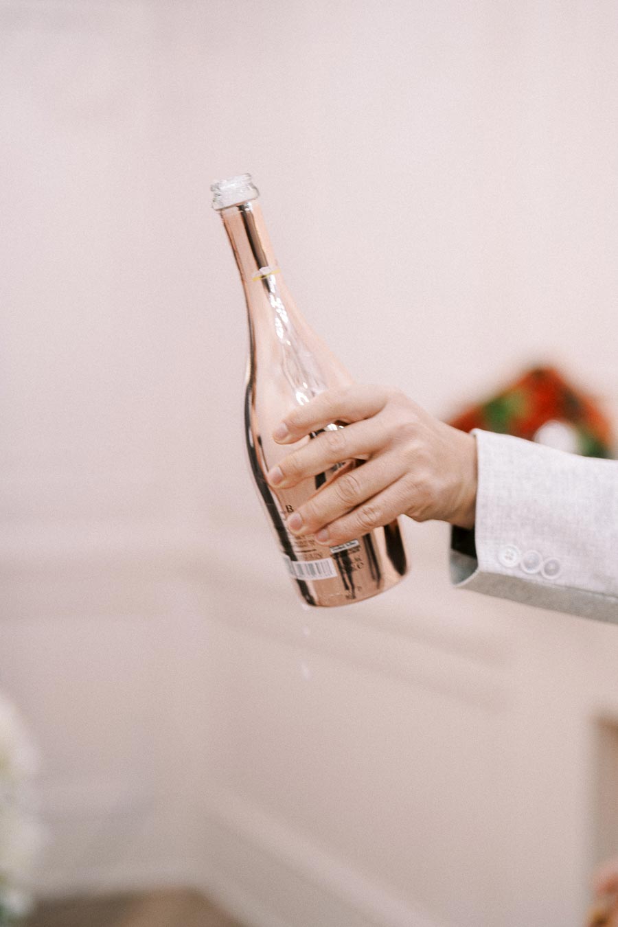 A hand holding a rose-gold champagne bottle with a blurred white background, capturing an elegant and celebratory moment.