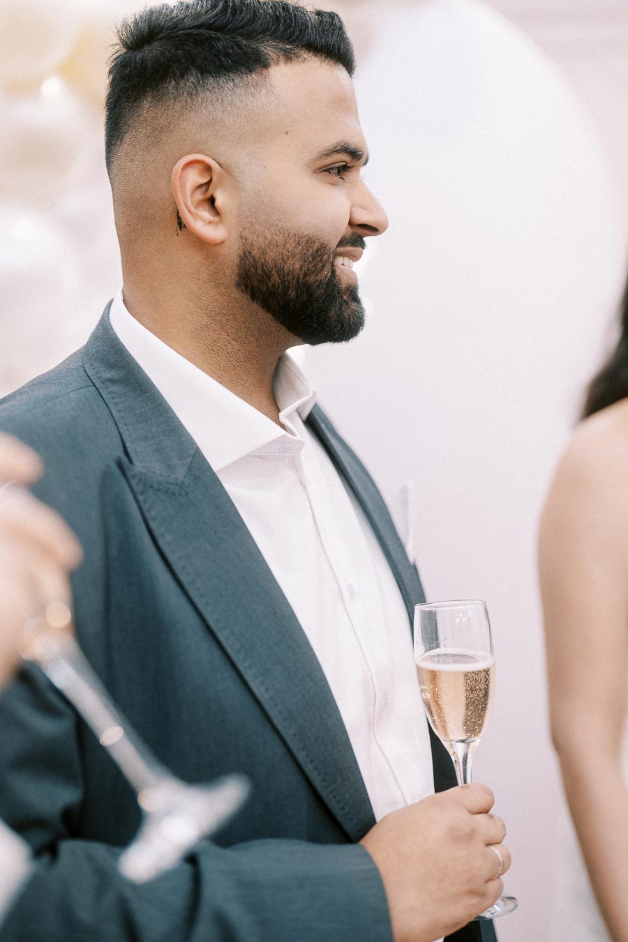 A man in a formal suit holding a champagne flute, enjoying a celebration or social event.
