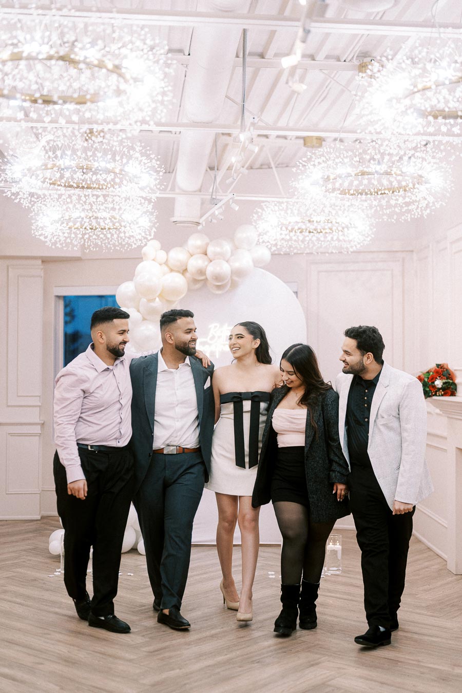 Group of friends celebrating at a stylish indoor event with elegant lighting and balloon decorations, dressed in formal attire.