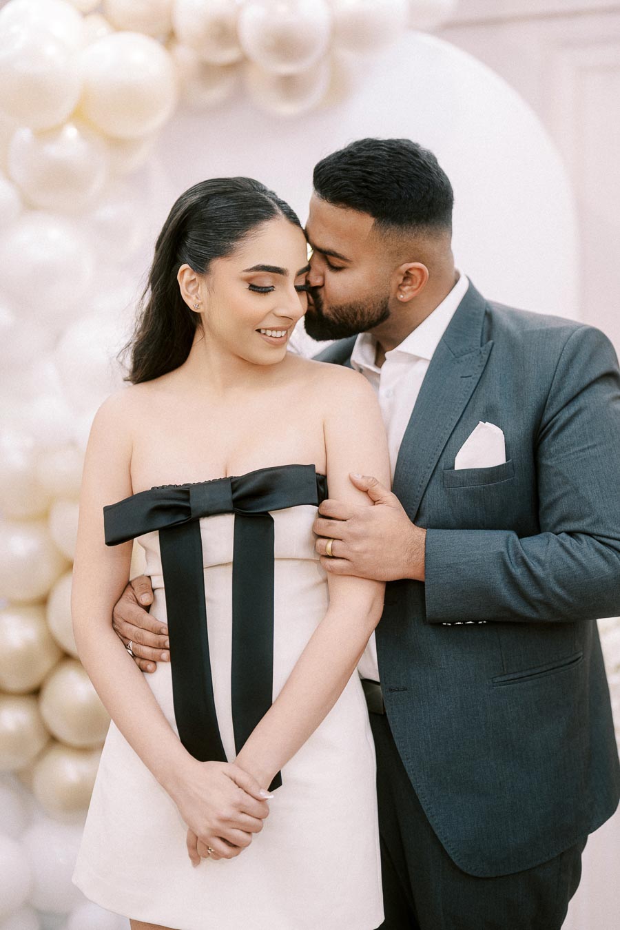 Romantic couple embracing at an elegantly decorated event with a white balloon backdrop.