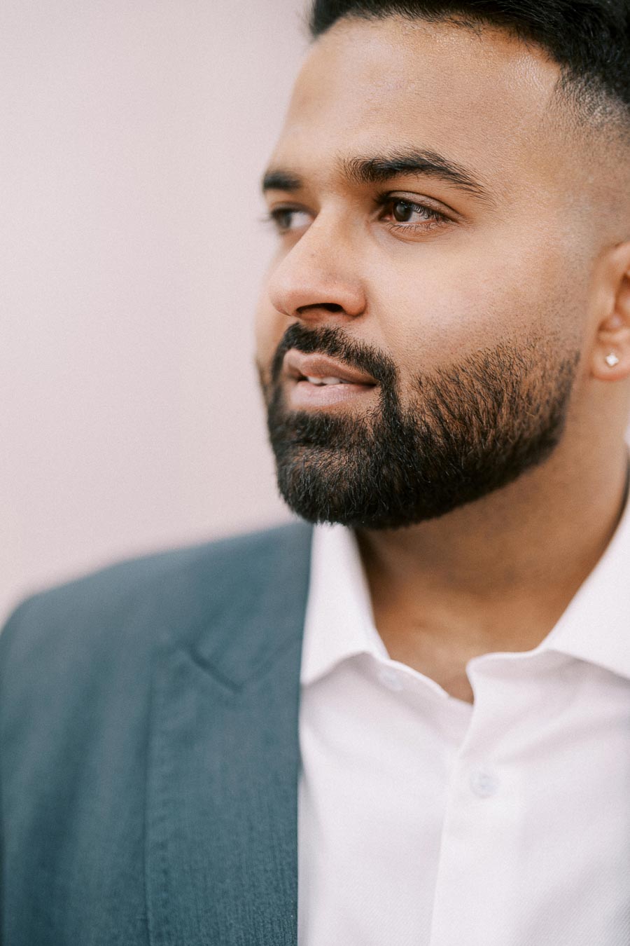 A person in a suit glancing sideways, showcasing a neatly trimmed beard and professional attire.