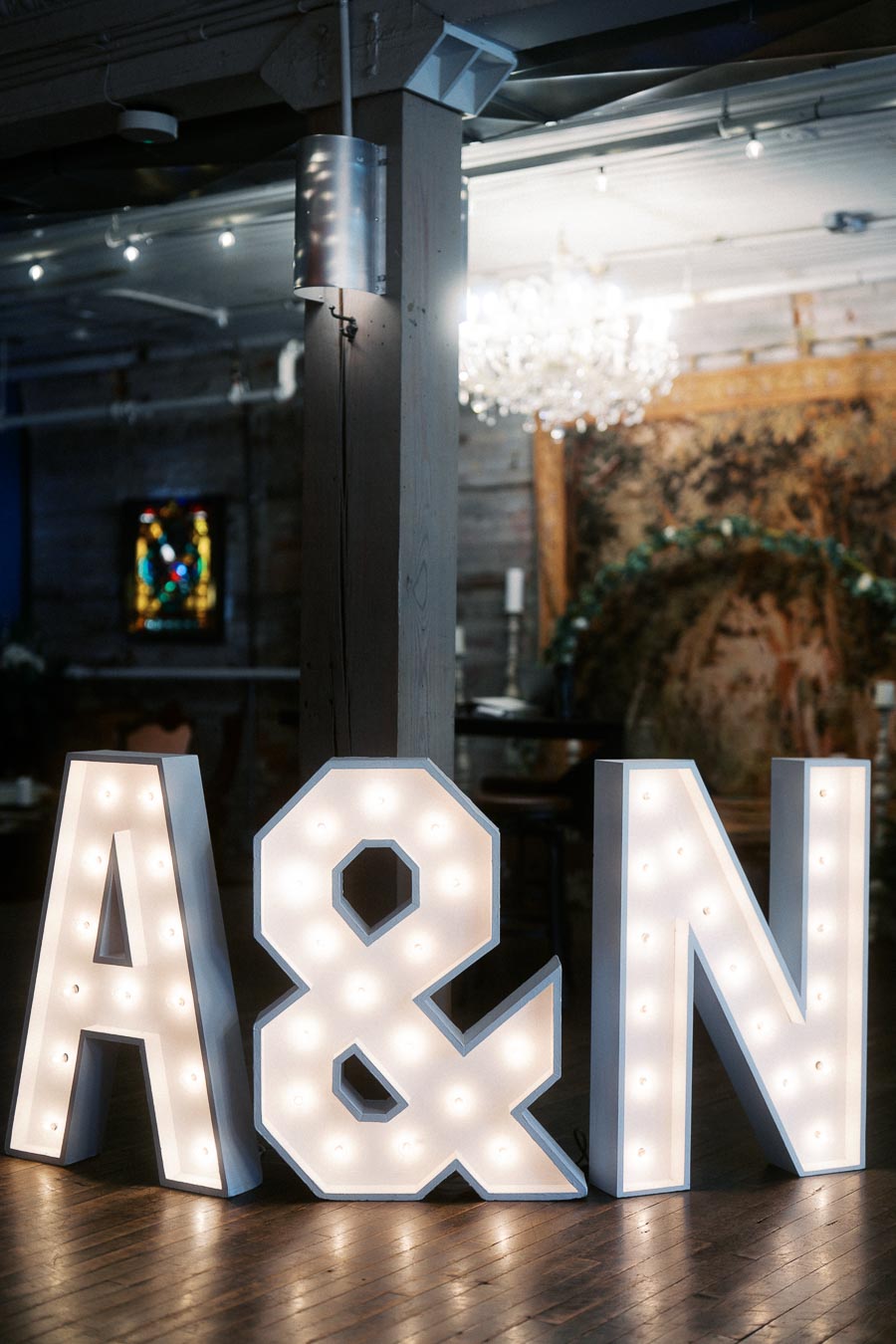 Illuminated marquee letters A & N in a dimly lit rustic indoor setting with wooden floors and decorative background elements.