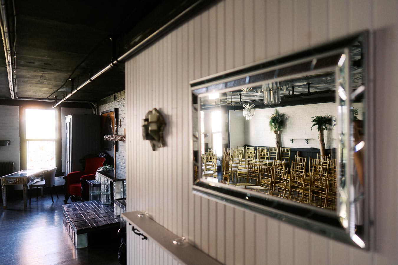 Modern and elegant interior space with reflection in a wall-mounted mirror, showcasing rows of gold chairs and decorative plants, suitable for events or gatherings.
