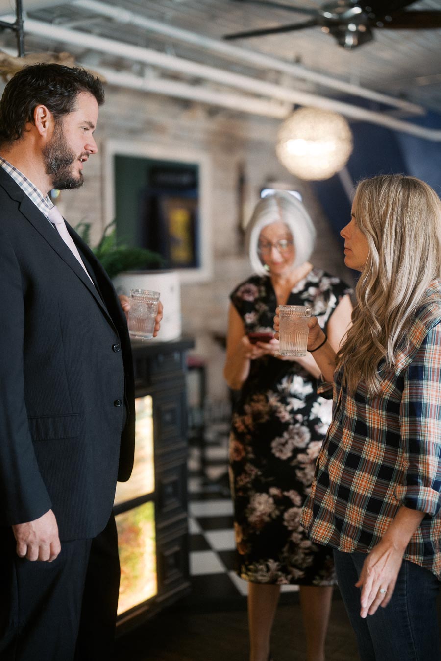 A group of people engaging in conversation at a casual gathering, holding drinks, with a blurred background of a cozy, indoor setting.