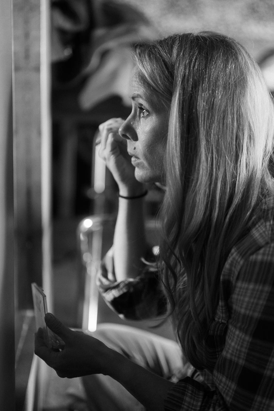 A woman in a plaid shirt applying makeup in front of a mirror, captured in a black and white photograph, emphasizing a moment of introspection and self-care.