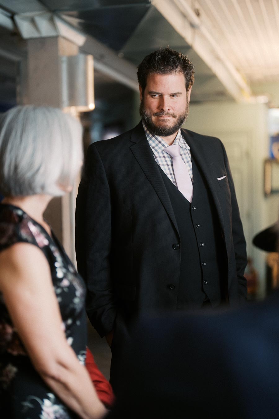 Man in a suit with a pink tie making eye contact with a woman at an indoor social gathering.