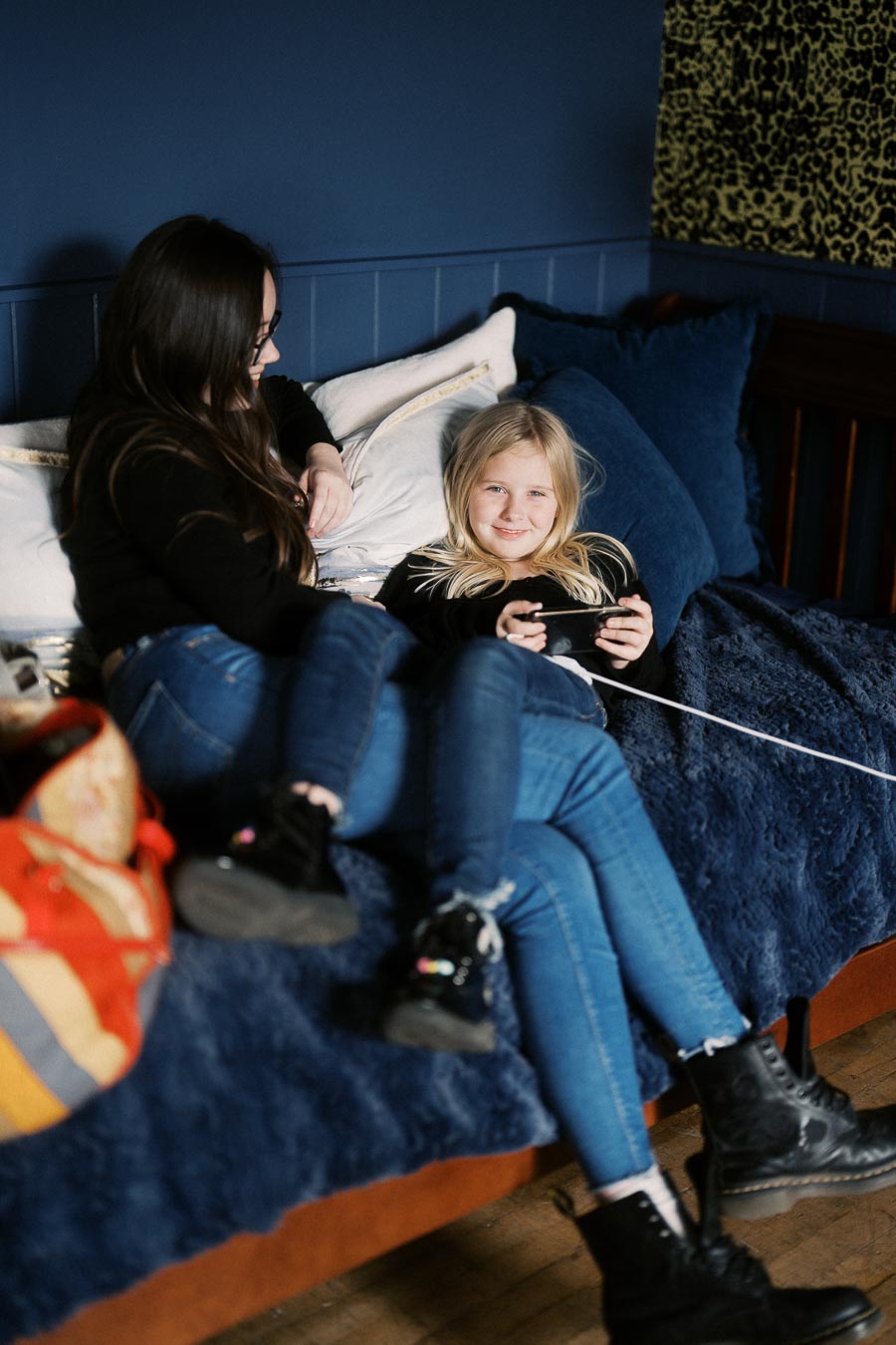 Mother and daughter enjoying quality time playing video games on a cozy sofa with a blue blanket and pillows in a warmly decorated living room.