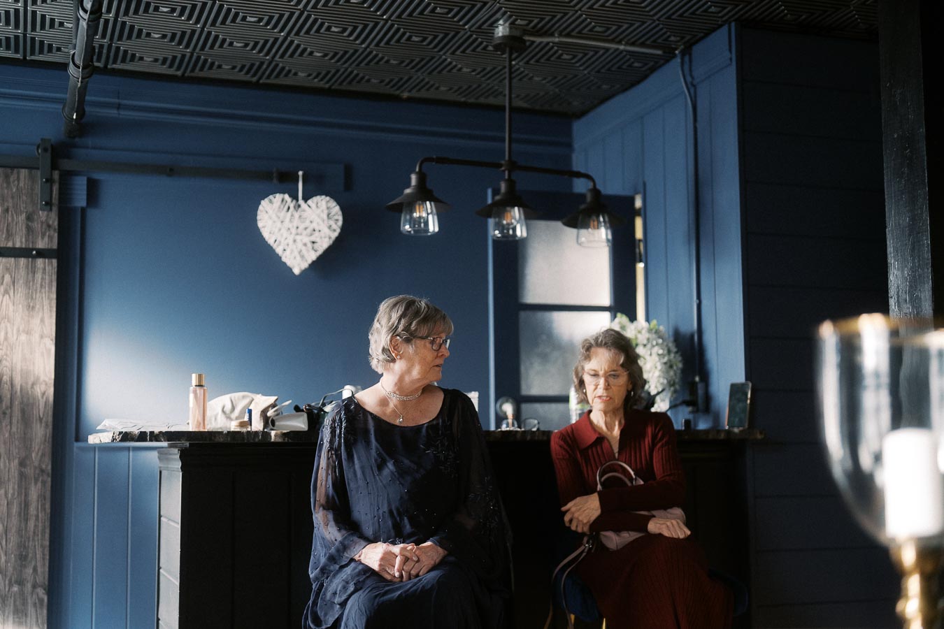 Elderly women seated in a stylish, modern room with blue walls and decorative elements, engaged in conversation, under elegant lighting.