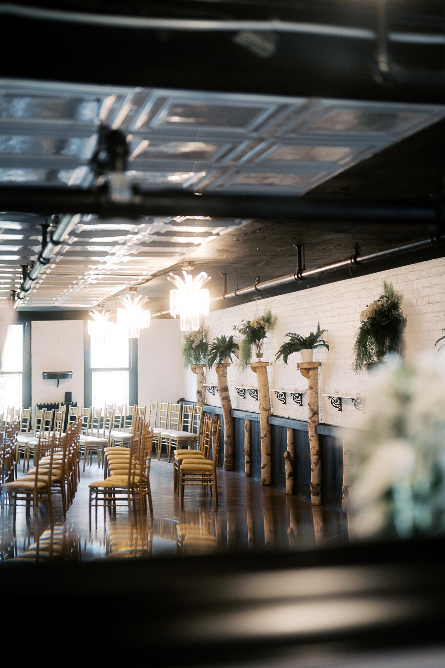 Elegant event space with rows of wooden chairs, greenery decor on the walls, and modern ceiling lights, ideal for weddings or corporate gatherings.