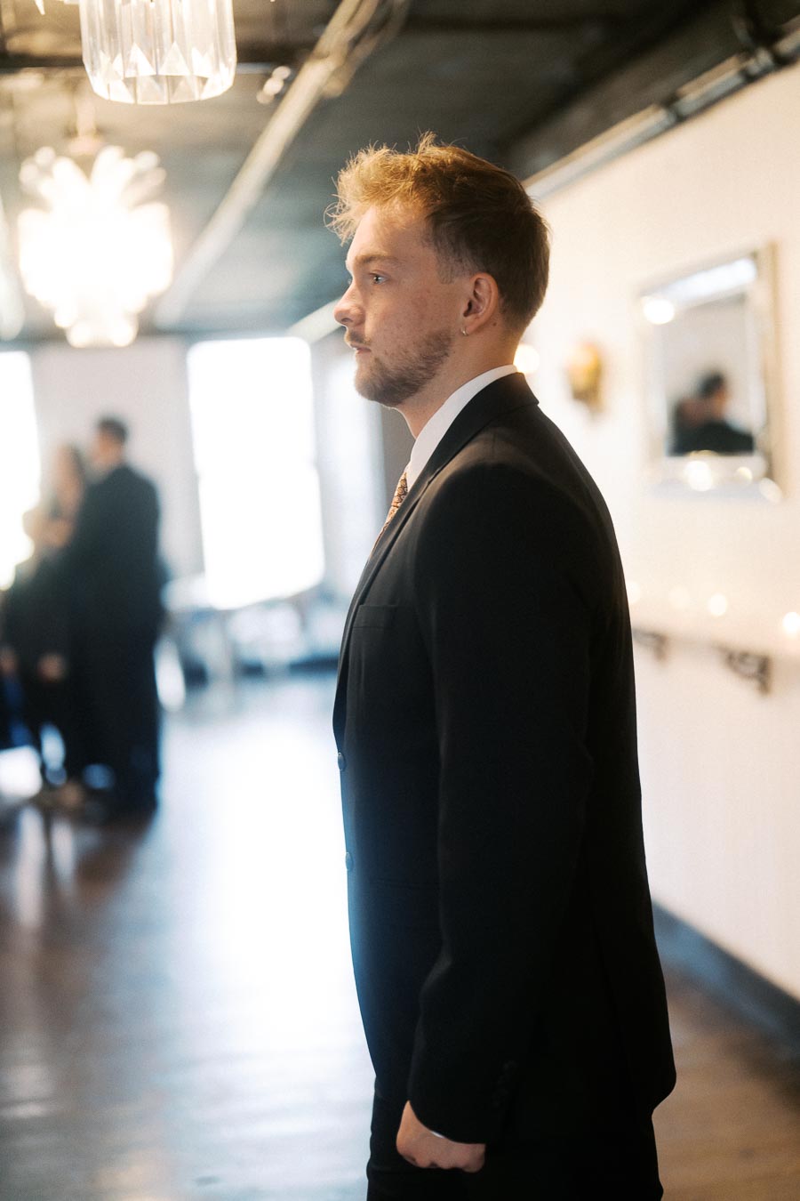 A young man in a suit stands confidently in a well-lit, stylish interior, embodying professionalism and modern elegance.